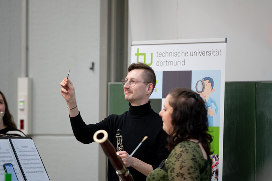 Ein junger Mann mit Brille hält das Rohrblatt seiner Oboe hoch.