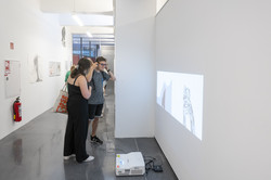 Rundgang Kunst Videoprojektion Ein Mann mit Kopfhörern und eine Frau stehen vor einem Beamer, der vom Boden aus ein Video an die Wand projeziert.