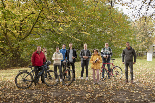 Eine Gruppe von Menschen steht mit Fahrrädern auf einer Wiese mit viel Laub.