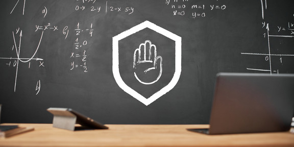Im Vordergrund stehen ein Laptop und ein Tablet auf einem Tisch, im Hintergrund ist eine Tafel. Darauf sind in stilisierter Form eine ausgestreckte Hand in einem Schutzschild zu sehen.