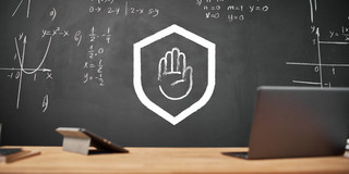 Im Vordergrund stehen ein Laptop und ein Tablet auf einem Tisch, im Hintergrund ist eine Tafel. Darauf sind in stilisierter Form eine ausgestreckte Hand in einem Schutzschild zu sehen.