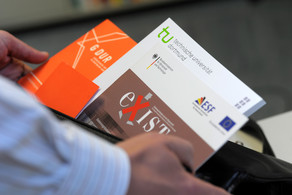 A man's hands are holding flyers of TU Dortmund University
