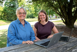 Zwei Frauen sitzen draußen an einem Tisch mit Laptops.