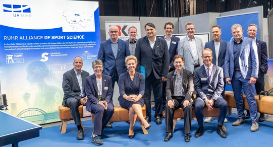 Gruppenbild mit mehreren Personen vor einer Veranstaltungswand.