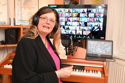 Frau mit Kopfhörern auf den Ohren sitzt vor einem Klavier. Im Hintergrund zwei Computerbildschirme