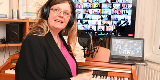Frau mit Kopfhörern auf den Ohren sitzt vor einem Klavier. Im Hintergrund zwei Computerbildschirme