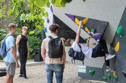 Foto: Ein Student klettert an einem Boulder-Felsen. Drei andere Studenten schauen ihm dabei zu.