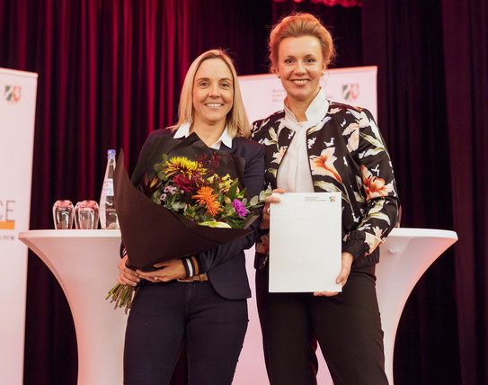 NRW-Wissenschaftsministerin überreicht Dr. Vanessa Henke Blumen und Urkunde