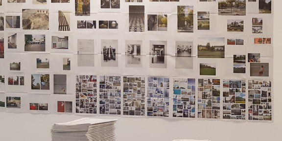 Fotos hängen in einer Ausstellung an der Wand, im Vordergrund liegt ein Stapel Zeitungen