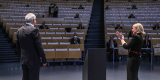 A woman and a man stand on a stage. A few people sit in the audience.