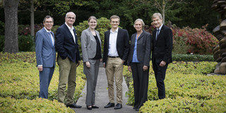 Gruppenfoto von sechs Personen, die in eleganter Kleidung in einem Park posieren.