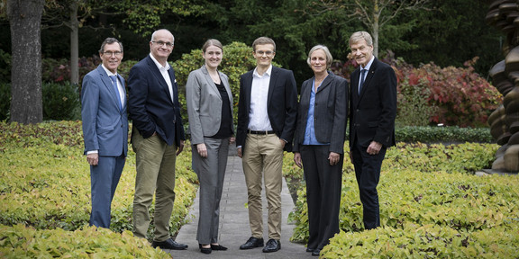 Gruppenfoto von sechs Personen, die in eleganter Kleidung in einem Park posieren.