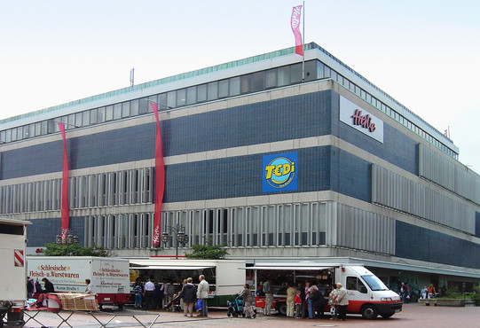 Großes Kaufhaus. Im Vordergrund findet ein Markt statt.