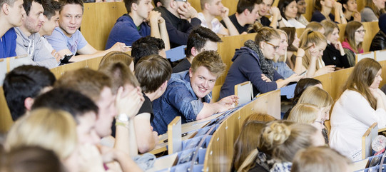 Gruppe von Studierenden im Hörsaal, Im Fokus ein junger Mann der lacht