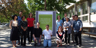 A group photo in front of a building and in front of a poster for the conference.