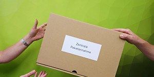 Paketannahme Ein Paket wird zwischen zwei Personen weiter gereicht.
