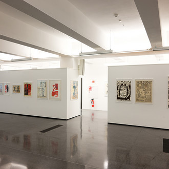 Das Bild zeigt einen Ausstellungsraum mit verschiedenen internationalen Künstlerplakaten an einer weißen Wand.