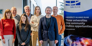 Foto: Ein Gruppenfoto vom UA Ruhr Rat für Ethik und Verantwortung neben einem Aufsteller der UA Ruhr. Auf dem Aufsteller steht: "University Alliance Ruhr. Three universities, one community, endless opportunities""