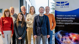 Foto: Ein Gruppenfoto vom UA Ruhr Rat für Ethik und Verantwortung neben einem Aufsteller der UA Ruhr. Auf dem Aufsteller steht: "University Alliance Ruhr. Three universities, one community, endless opportunities""