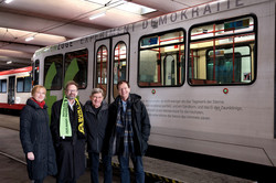 Four people stand in front of a train on which a Whitman quote is printed.
