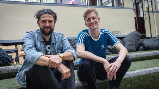 Zwei Männer sitzen nebeneinander am Wegrand.