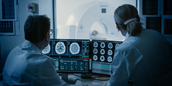 A man and a woman sit in the control room during an MRI and watch the images on a screen.