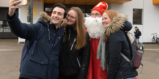 Drei Studierende machen ein Selfie mit einem Mann, der als Nikolaus verkleidet ist.