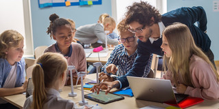 Foto: Ein Mann zeigt einer Gruppe Kinder am Tisch Inhalte auf einem Tablet.