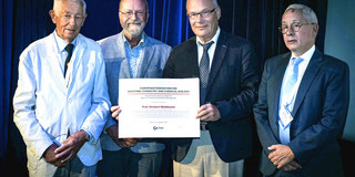 Prof. Herbert Waldmann stands on a stage with three other men. In his hands he holds the Nauta Prize.