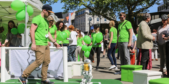 Fußballroboter Menschen stehen um ein Spielfeld von Fußballrobotern.
