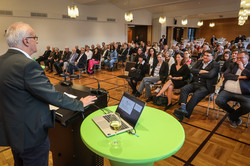 Mann steht am Rednerpult mit Blick auf Gäste im Saal