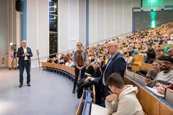 A man in the audience of the packed lecture hall asks a question