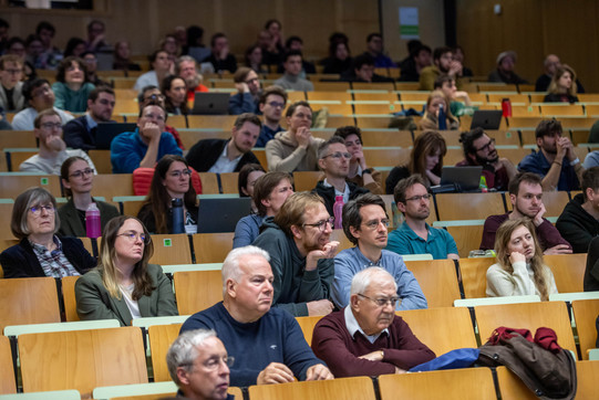 Das Bild zeigt sitzende Zuhörende in Hörsaalreihen.