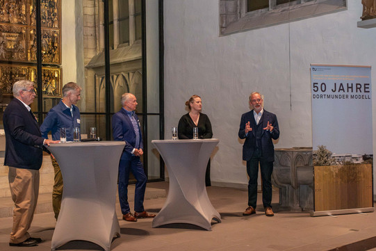 Das Bild zeigt vier Männer und eine Frau in der St. Petri Stadtkirche in Dortmund. Außerdem stehen vor ihnen zwei Stehtische. Im Hintergrund sieht man den Altar.