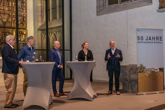 Das Bild zeigt vier Männer und eine Frau in der St. Petri Stadtkirche in Dortmund. Außerdem stehen vor ihnen zwei Stehtische. Im Hintergrund sieht man den Altar.