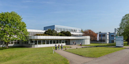 Foto: Das Gebäude des Frauenhofer IML an einem sonnigen Tag. Das Gebäude ist flach und weiß und von Gründflächen umgeben.
