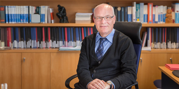 Prof. Waldmann is sitting at a desk surrounded by books.