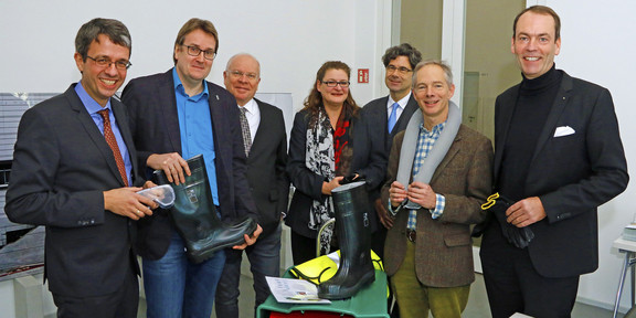 Gruendung-Notfallverbund Das Bild zeigt sieben Menschen. Einige von ihnen halten verschiedene Gegenstände in der Hand, die für den gegründeten Notfallverbund von Belang sind, beispielsweise Gummistiefel oder eine Schutzbrille.