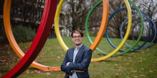 A portrait of a man, Prof. Lukas Buchheim, outside in front of colorful large steel rings.