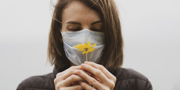Eine Frau trägt eine Maske und hält eine Blume in der Hand.
