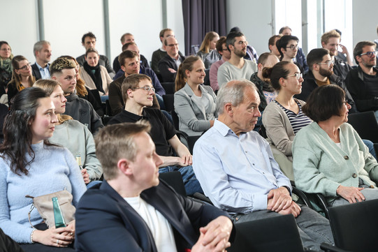 Mehrere Personen sitzen auf Stühlen und blicken in die selbe Richtung.