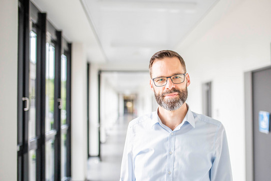 Portraitbild eines Mannes mit Brille auf dem Gang eines Bürogebäudes.