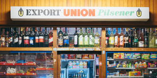 Zu sehen ist ein Kioskschaufenster mit einer Leuchtreklame "Export, Union, Pilsner" steht.