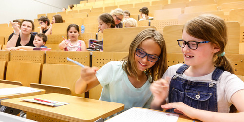 Kinder sitzen in den Reihen eines Hörsaals und bearbeiten Mathematikaufgaben mit Spaß und Spannung - Trickspiele 