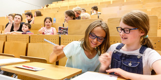 KinderUni-Hörsaal Kinder sitzen in den Reihen eines Hörsaals und bearbeiten Mathematikaufgaben mit Spaß und Spannung - Trickspiele