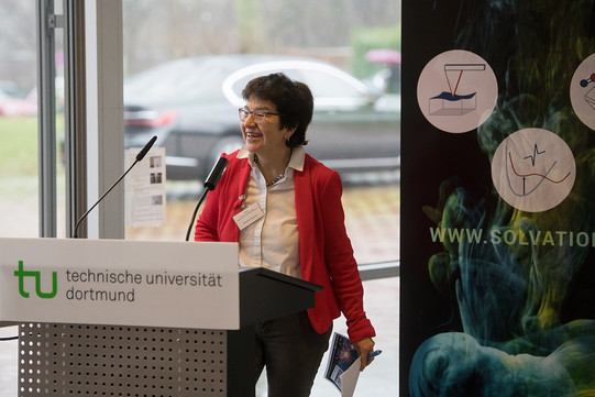 A woman in a red blazer stands at a lectern
