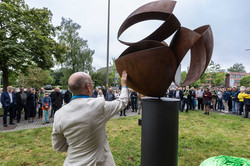 Einweihung Skulptur Ein Mann in hellem Anzug (Sebastian Wien) zeigt vor einem großen Publikum auf seine bronzefarbene, rundliche Skulptur