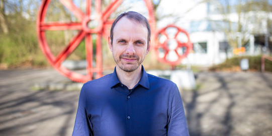 Porträtfoto von Prof. Marcel Bartz: Prof. Bartz steht auf dem Campus der TU Dortmund. Er trägt ein blaues Hemd.