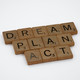 Mit Buchstaben aus dem Spiel Scrabble liegen die Wörter Dream, Plan und Act auf einem weißen Untergrund.