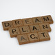 Mit Buchstaben aus dem Spiel Scrabble liegen die Wörter Dream, Plan und Act auf einem weißen Untergrund.